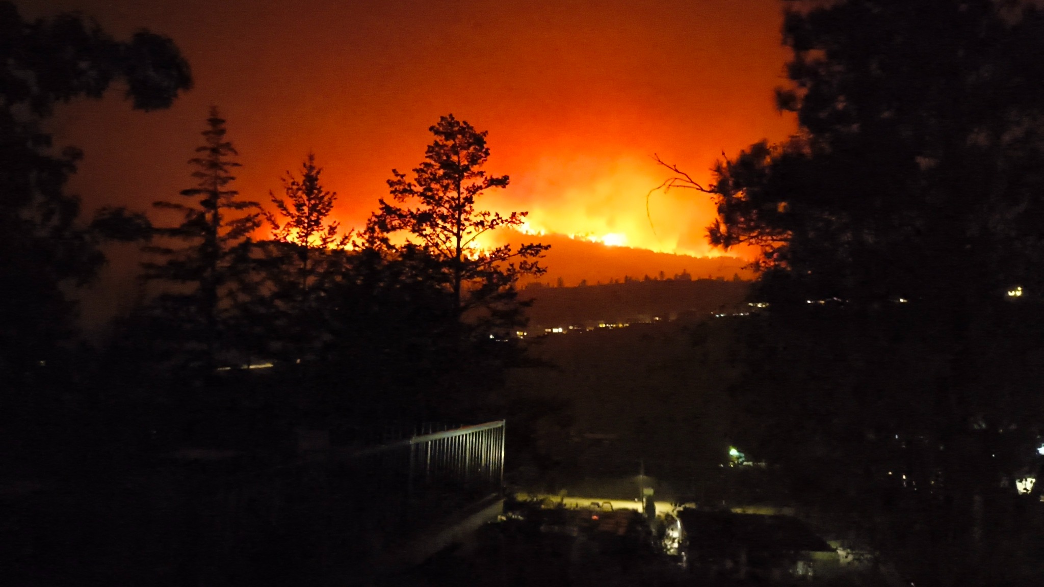 Wildfire line visible at night beyond homes and trees in Summerland